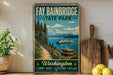 A vintage-style sign for Fay Babinbridge State Park, featuring a scenic image of a path leading to a picnic area with a boat on the water, surrounded by pine trees and mountains.