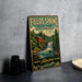 A vintage-style metal sign for "Fields Spring State Park, Washington" featuring a waterfall and a red cabin, placed on a gray countertop next to some black camera lenses.