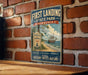 a vintage-style metal sign with a ship and beach scene, mounted on a brick wall.