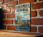 A vintage metal sign for Fishermen's Memorial State Park, featuring a lighthouse and a monument, mounted on a brick wall.