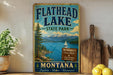 A vintage-style sign for Flathead Lake State Park in Montana, featuring a scenic landscape with mountains, a lake, and a sailboat.