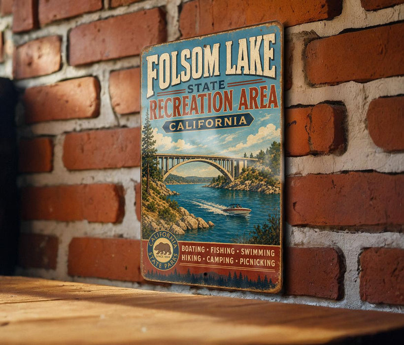 A vintage metal sign for Folsom Lake State Recreation Area in California, featuring a scenic illustration of a bridge over a river with boats and people enjoying the outdoors.