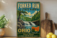 A vintage-style sign for Forked Run State Park in Ohio, featuring a scenic image of a waterfall surrounded by trees and mountains.