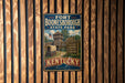 A vintage metal sign for Fort Booneborough State Park in Kentucky, featuring a wooden fort and a wagon, mounted on a wooden wall.