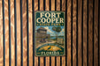 A vintage metal sign for Fort Cooper State Park in Florida, featuring a wooden structure and palm trees, mounted on a wooden wall.