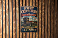 A vintage-style metal sign for the Fort Creve Coeur State Historic Site in Illinois, featuring an illustration of a historic building and a banner that reads "Discovery Illinois History Illinois".
