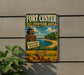 A vintage-style metal sign for Fort Custer Recreation Area, featuring a beach scene and a lighthouse, is mounted on a gray wall.