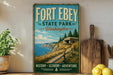 A vintage-style sign for Fort Ebey State Park in Washington, featuring a scenic coastal landscape with a lighthouse and a wooden fence.
