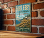 A vintage-style metal sign for Fort Ebey State Park in Washington, featuring a scenic landscape with a path leading to a building and a body of water.