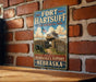 A vintage-style metal sign for Fort Hartsuff State Historical Park in Nebraska, featuring an illustration of a historical fort and a wooden fence.