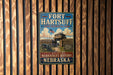 A vintage-style metal sign for Fort Hartsuff State Historical Park in Nebraska, featuring an illustration of a wooden fort and a cannon.