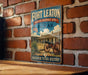 A vintage-style metal sign for the Fort Leaton State Historic Site in Texas, featuring an illustration of a cannon and a house, mounted on a brick wall.