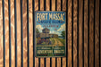 A vintage metal sign for Fort Massac State Park in Illinois, featuring a cannon and a wooden fence, hangs on a wooden wall.
