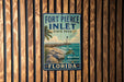 A vintage-style metal sign for Fort Pierce Inlet State Park in Florida, featuring a beach scene with a lighthouse and palm trees.