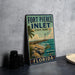 A vintage-style sign for Fort Pierce Inlet State Park in Florida, featuring a beach scene with palm trees, a lighthouse, and a turtle.