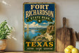 A vintage-style sign for Fort Richardson State Park in Texas, featuring a scenic landscape with a river, mountains, and a desert.