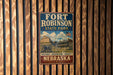 A vintage-style metal sign for Fort Robinson State Park in Nebraska, featuring an illustration of a historic building and a horse-drawn carriage.