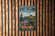 A vintage metal sign for Fort Snelling State Park in Minnesota, featuring a cannon, a building, and a lake, mounted on a wooden wall.