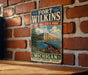 A vintage-style metal sign for Fort Wilkins Historic State Park in Michigan, featuring an illustration of a cannon and a building, mounted on a brick wall.