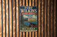 A vintage metal sign for Fort Wilkins Historic State Park in Michigan, featuring an illustration of a cannon and a building, mounted on a wooden wall.