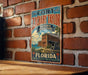 A vintage-style metal sign for Fort Zachary Taylor Historic State Park in Florida, featuring a brick wall and palm trees in the background.