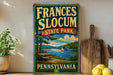a vintage-style sign for Frances Slocum State Park in Pennsylvania, with a scenic illustration of a lake, trees, and a sailboat.
