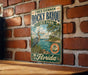 A vintage-style metal sign for Rocky Bayou State Park in Florida, featuring a scenic illustration of the bayou and its surroundings.
