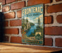 A vintage metal sign for Frontenac State Park in Minnesota, featuring a scenic landscape with a lake, mountains, and pine trees.