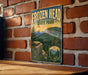 A vintage-style sign for Frozen Head State Park, featuring a scenic mountain landscape with pine trees and a sunset in the background.