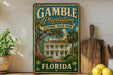 A vintage-style metal sign for Gamble Plantation Historic State Park in Florida, featuring a large illustration of a historic house surrounded by palm trees and other tropical foliage.