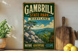 A vintage-style metal sign for Gambrill State Park, Maryland, featuring a scenic mountain landscape with pine trees and rocky outcroppings.