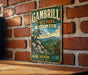 A vintage metal sign for Gambrill State Park, Maryland, featuring a scenic mountain landscape with a pine tree and rocks.