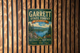 A vintage metal sign for Garrett State Forest, Maryland, mounted on a wooden wall.