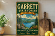A vintage-style sign for Garrett State Forest, Maryland, featuring a scenic landscape with pine trees, a lake, and mountains.