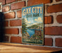 A vintage metal sign for Gay City State Park in Connecticut, featuring a scenic landscape with a lake and mountains.
