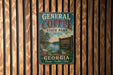 A vintage-style metal sign for General Coffee State Park in Georgia, featuring a scenic landscape with a lake and trees.