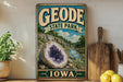 A vintage-style sign for Geode State Park in Iowa, featuring a large purple geode and a scenic landscape.
