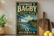A vintage-style metal sign for George T. Bagby State Park in Georgia, featuring a scenic landscape with a lake, forest, and waterfall.