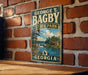 A vintage-style metal sign for George T. Bagby State Park in Georgia, featuring a scenic landscape with a lake and a small cabin.