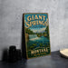 A vintage-style sign for the state park called "Giant Springs State Park" in Montana, featuring a scenic image of a waterfall and mountains.