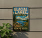 A vintage-style metal sign for Glacier Lakes State Park in Minnesota, featuring a scenic landscape with a lake, mountains, and pine trees.