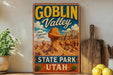 A vintage-style sign for Goblin Valley State Park in Utah, featuring a desert landscape with a large rock formation.