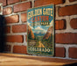 A vintage-style sign for Golden Gate Canyon State Park in Colorado is displayed on a brick wall.