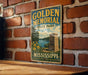A vintage-style metal sign for Golden Memorial State Park in Mississippi, featuring a scenic landscape with a lake, trees, and a monument.