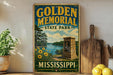 A vintage-style sign for Golden Memorial State Park in Mississippi, featuring a scenic landscape with a river, trees, and a stone monument.