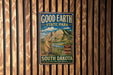 A metal sign with a mountain landscape and a meadow with a beaver, mounted on a wooden fence.