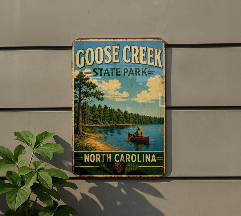 A vintage-style sign for Goose Creek State Park in North Carolina, featuring a scenic image of a person canoeing on a lake surrounded by pine trees.