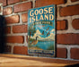 A vintage-style metal sign for Goose Island State Park in Texas, featuring a goose and palm trees, is mounted on a brick wall.