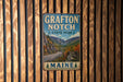 A vintage metal sign for Grafton Notch State Park in Maine, featuring a scenic mountain landscape.