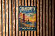 A vintage-style metal sign for Grand Haven State Park in Michigan, featuring a lighthouse and a sunset over the ocean.